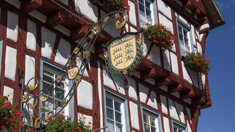 Fachwerkhaus in Bad Urach mit Schild 'Altes Oberamt' und blühenden Blumenkästen an den Fenstern., © Bad Urach Tourismus Fachwerkhaus in Bad Urach mit Schild 'Altes Oberamt' und blühenden Blumenkästen an den Fenstern., © Bad Urach Tourismus