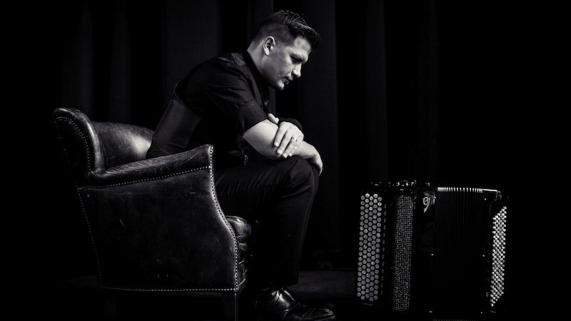 Ein Mann sitzt nachdenklich in einem Sessel neben einem Akkordeon in einem dunklen Raum. Die Szene ist in Schwarz-Wei&szlig; gehalten., &copy; Kulturhaus Schwanen