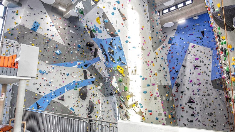 Kletterhalle mit hohen, bunten Wänden und Griffen. Im Vordergrund ein Sitzbereich mit orangen Kissen und Sesseln., © Griffwerk Ludwigsburg Kletterhalle mit hohen, bunten Wänden und Griffen. Im Vordergrund ein Sitzbereich mit orangen Kissen und Sesseln., © Griffwerk Ludwigsburg