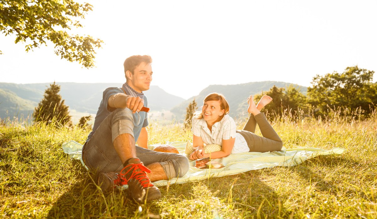 Ein Paar sitzt auf einer Decke bei einem Picknick auf einer sonnigen Wiese mit Bergblick., © Landkreis Göppingen Ein Paar sitzt auf einer Decke bei einem Picknick auf einer sonnigen Wiese mit Bergblick., © Landkreis Göppingen