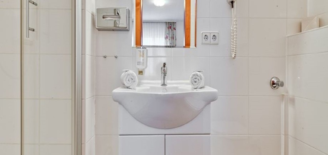 Ein modernes Badezimmer mit weißem Waschbecken, Spiegel, Haartrockner und Dusche. Handtücher sind ordentlich aufgerollt., © ARNOTEL GmbH Ein modernes Badezimmer mit weißem Waschbecken, Spiegel, Haartrockner und Dusche. Handtücher sind ordentlich aufgerollt., © ARNOTEL GmbH