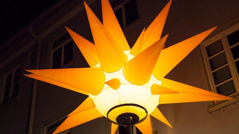 Eine gro&szlig;e, leuchtende gelbe Sternlampe mit spitzen Zacken h&auml;ngt vor einem Geb&auml;ude bei Nacht., &copy; Citymanagement