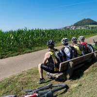 Drei Radfahrer mit Helmen sitzen auf einer Bank am Wegesrand, Fahrräder liegen daneben. Im Hintergrund ist der Hohenstaufen zu sehen., © Landkreis Göppingen Drei Radfahrer mit Helmen sitzen auf einer Bank am Wegesrand, Fahrräder liegen daneben. Im Hintergrund ist der Hohenstaufen zu sehen., © Landkreis Göppingen