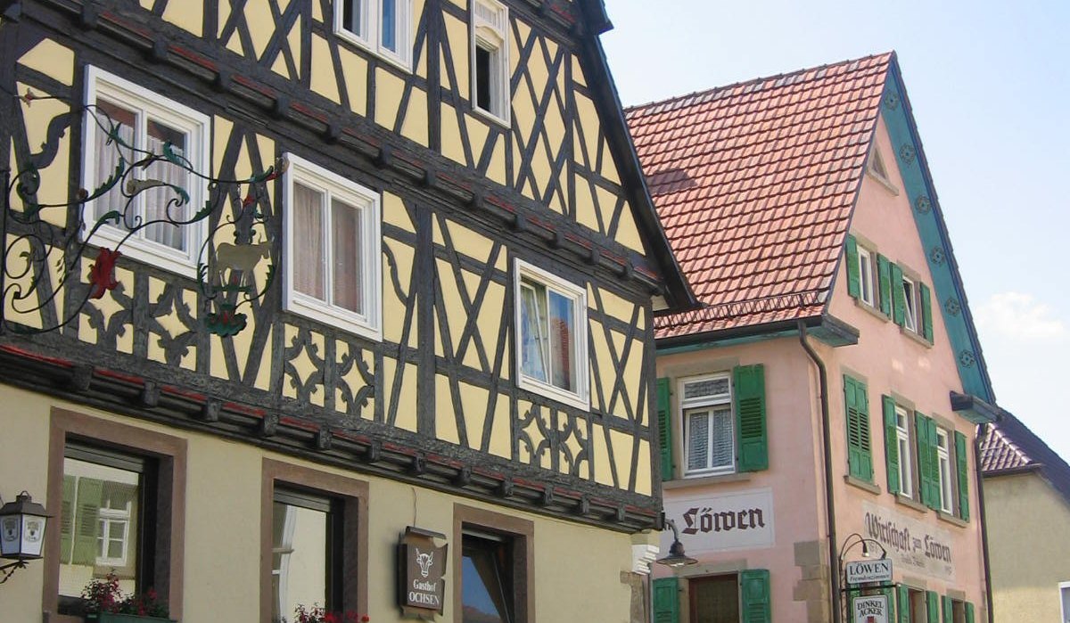 Fachwerkhäuser in einer deutschen Stadt. Links das Gasthaus 'Zum Ochsen', rechts 'Zum Löwen'. Beide Gebäude haben bunte Fensterläden., © Land der 1000 Hügel - Kraichgau-Stromberg