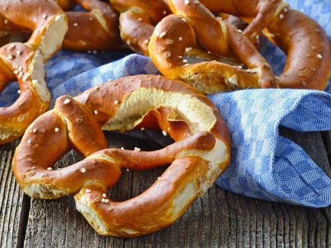 Frische Brezeln liegen auf einem blau-weiß karierten Tuch auf einem rustikalen Holztisch., © Cool-Tours StattReisen Frische Brezeln liegen auf einem blau-weiß karierten Tuch auf einem rustikalen Holztisch., © Cool-Tours StattReisen