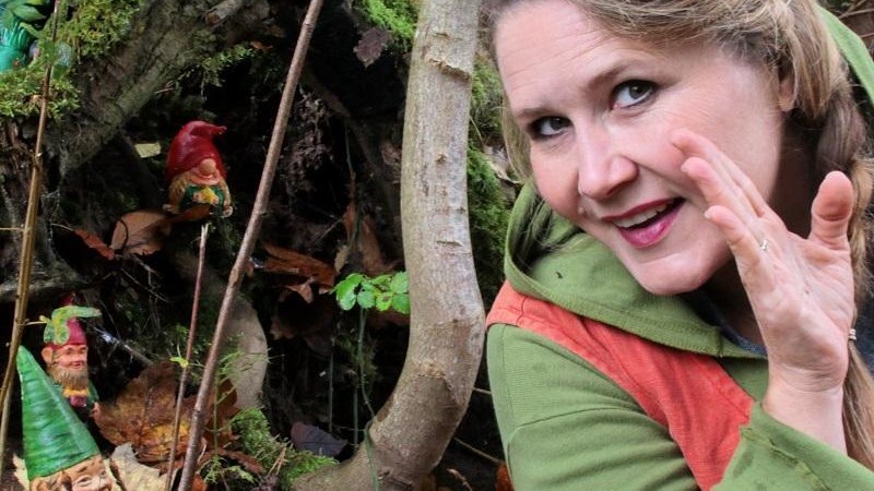 Eine Frau im Wald fl&uuml;stert zu kleinen Zwergenfiguren, die zwischen B&auml;umen und Moos versteckt sind. Sie tr&auml;gt gr&uuml;ne und orange Kleidung., &copy; Copyright: Stefanie Keller