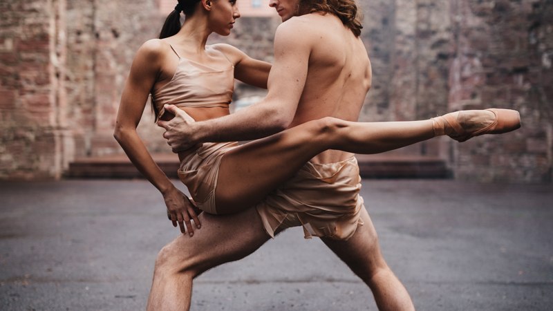 Zwei Balletttänzer in hautfarbenen Kostümen tanzen vor einer alten Steinruine. Eine Tänzerin wird elegant in die Luft gehoben., © Andrea D'Aquino Zwei Balletttänzer in hautfarbenen Kostümen tanzen vor einer alten Steinruine. Eine Tänzerin wird elegant in die Luft gehoben., © Andrea D'Aquino
