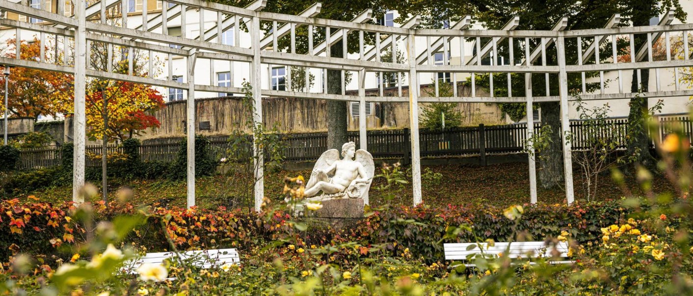 Eine Skulptur in einem herbstlichen Park, umgeben von buntem Laub und Blumen. Im Hintergrund sind wei&szlig;e Strukturen und Geb&auml;ude zu sehen., &copy; SMG, Sarah Schmid