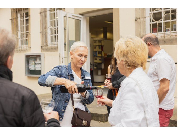 Eine Frau schenkt einer anderen Frau Wein ein. Zwei weitere Personen stehen im Hintergrund vor einem Geb&auml;ude., &copy; Eigenbetrieb Tourismus und Citymanagement Schorndorf