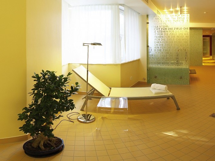 Heller Wellnessbereich mit Liegestuhl, Pflanze und dekorativer Glaswand. Entspannende Atmosphäre mit warmen Gelbtönen und moderner Einrichtung., © relexa Waldhotel Schatten Heller Wellnessbereich mit Liegestuhl, Pflanze und dekorativer Glaswand. Entspannende Atmosphäre mit warmen Gelbtönen und moderner Einrichtung., © relexa Waldhotel Schatten