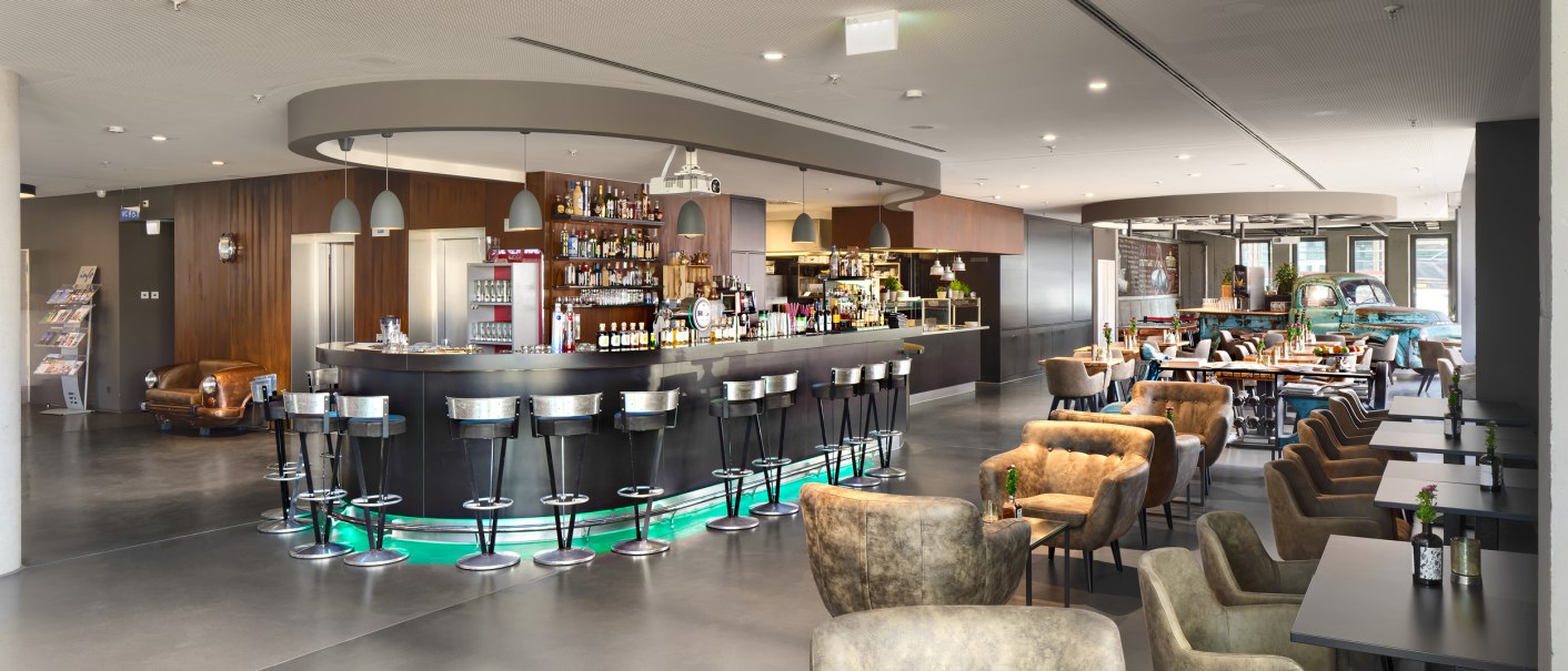 Moderne Hotelbar mit eleganten Barhockern, gemütlichen Sesseln und Tischen in einem offenen, stilvollen Raum., © V8 Hotel, Frank Hoppe Moderne Hotelbar mit eleganten Barhockern, gemütlichen Sesseln und Tischen in einem offenen, stilvollen Raum., © V8 Hotel, Frank Hoppe