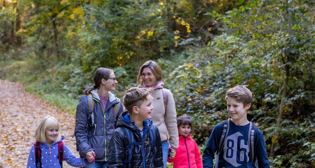 Eine Familie wandert auf einem Waldweg im Herbst. Die Erwachsenen und Kinder tragen Jacken und Rucksäcke. Der Boden ist mit Laub bedeckt., © Fotograf Thomas Zehnder Eine Familie wandert auf einem Waldweg im Herbst. Die Erwachsenen und Kinder tragen Jacken und Rucksäcke. Der Boden ist mit Laub bedeckt., © Fotograf Thomas Zehnder