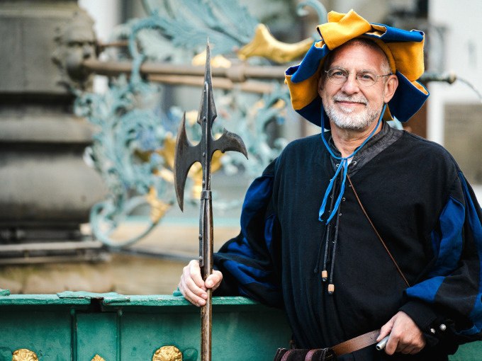 Ein Mann in historischer Kleidung mit Hellebarde posiert l&auml;chelnd vor einem kunstvoll verzierten Brunnen., &copy; Stadt N&uuml;rtingen