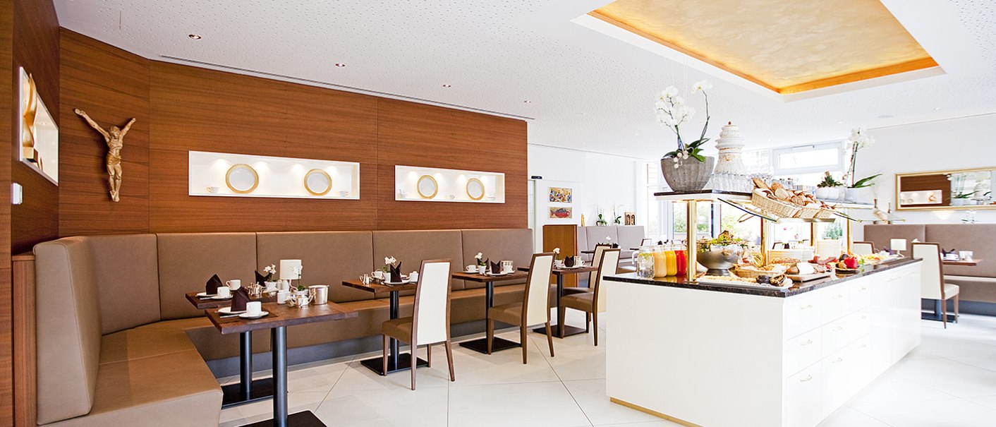 Ein heller Frühstücksraum mit modernem Design, Buffet und gemütlichen Sitzbereichen. Holzwände und dekorative Elemente schaffen eine einladende Atmosphäre., © Hotel Krone Ein heller Frühstücksraum mit modernem Design, Buffet und gemütlichen Sitzbereichen. Holzwände und dekorative Elemente schaffen eine einladende Atmosphäre., © Hotel Krone