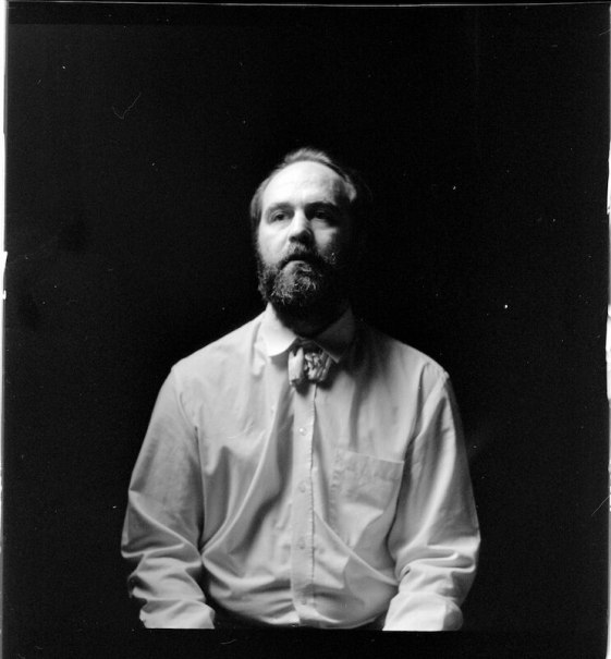 Schwarz-weiß Porträt eines bärtigen Mannes in Hemd und Fliege vor dunklem Hintergrund., © Kulturhaus Schwanen