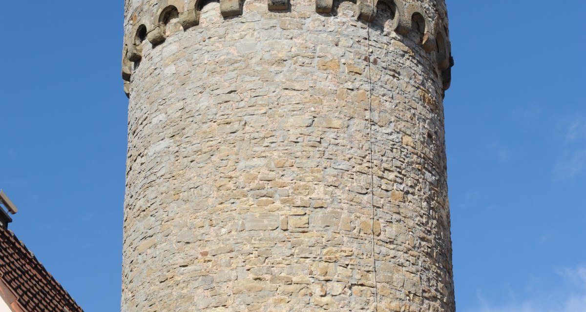 Ein runder Steinturm mit rotem Spitzdach, umgeben von Gebäuden, vor klarem blauem Himmel., © Land der 1000 Hügel - Kraichgau-Stromberg Ein runder Steinturm mit rotem Spitzdach, umgeben von Gebäuden, vor klarem blauem Himmel., © Land der 1000 Hügel - Kraichgau-Stromberg