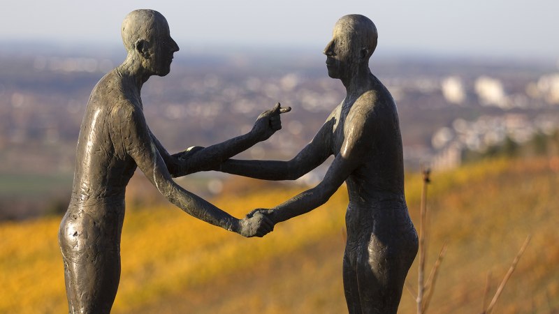 Zwei Bronzeskulpturen halten sich die Hände auf einem Hügel. Der Hintergrund ist unscharf und zeigt eine Landschaft., © SMG, Achim Mende