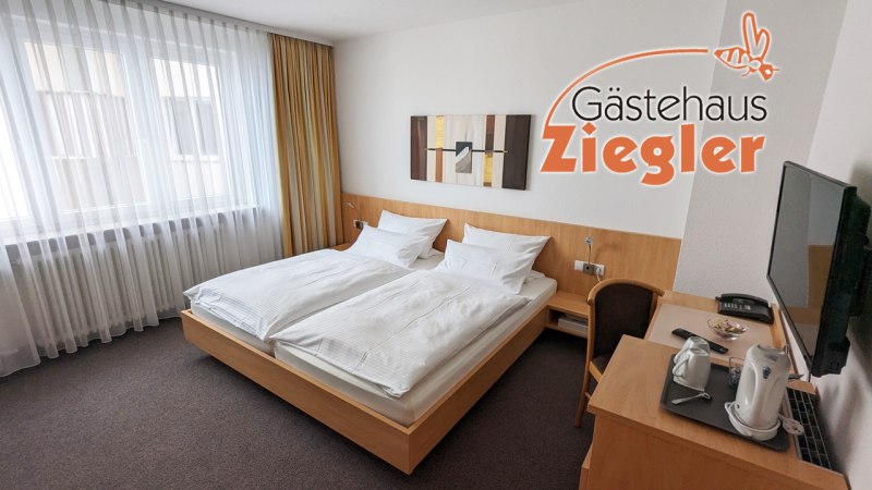 Helles Hotelzimmer mit Doppelbett, Schreibtisch, Fernseher und Wasserkocher im Gästehaus Ziegler. Moderne Dekoration und große Fenster mit Vorhängen., © Gästehaus Ziegler