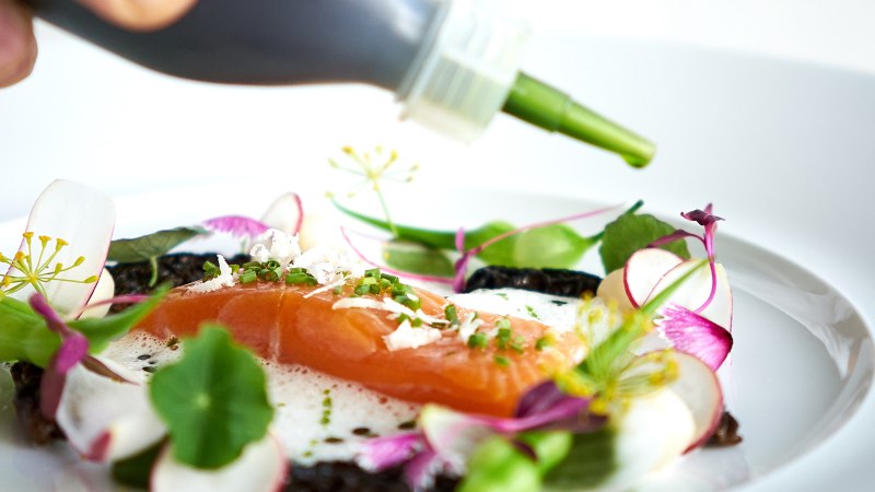 Ein Gourmetgericht mit Lachs, essbaren Blumen und grüner Sauce auf einem weißen Teller, kunstvoll angerichtet., © Stuttgart-Marketing GmbH, Annette Sandner Ein Gourmetgericht mit Lachs, essbaren Blumen und grüner Sauce auf einem weißen Teller, kunstvoll angerichtet., © Stuttgart-Marketing GmbH, Annette Sandner