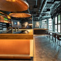 Modernes Caf&eacute; mit Bar, beleuchteten Regalen voller Flaschen, Gl&auml;sern und Sitzbereichen. Gro&szlig;e Fenster lassen viel Licht herein., &copy; Maks Richter