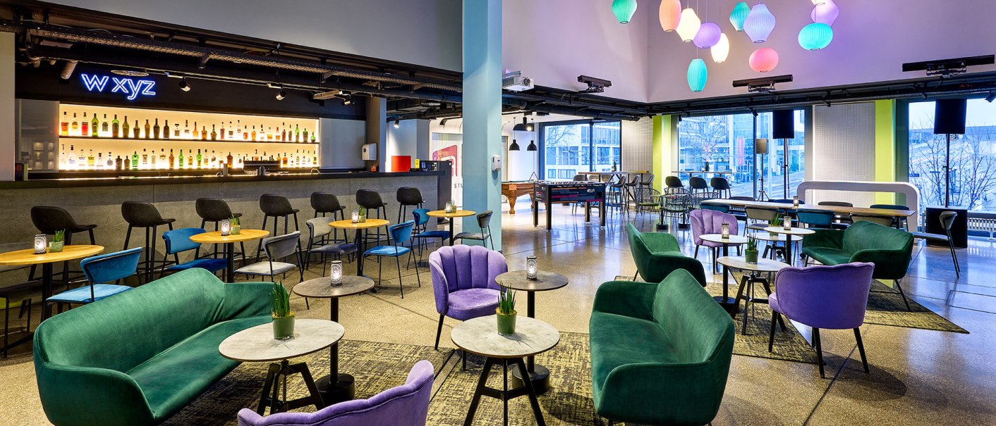 Moderne Lounge mit bunten Sesseln und Sofas, stilvoller Bar und farbenfrohen Lampen. Gro&szlig;e Fenster bieten Blick nach drau&szlig;en., &copy; aloft Stuttgart