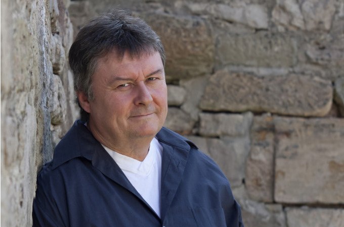 Ein Mann in dunkler Kleidung lehnt lächelnd an einer alten Steinmauer und blickt in die Kamera., © WTM GmbH Waiblingen