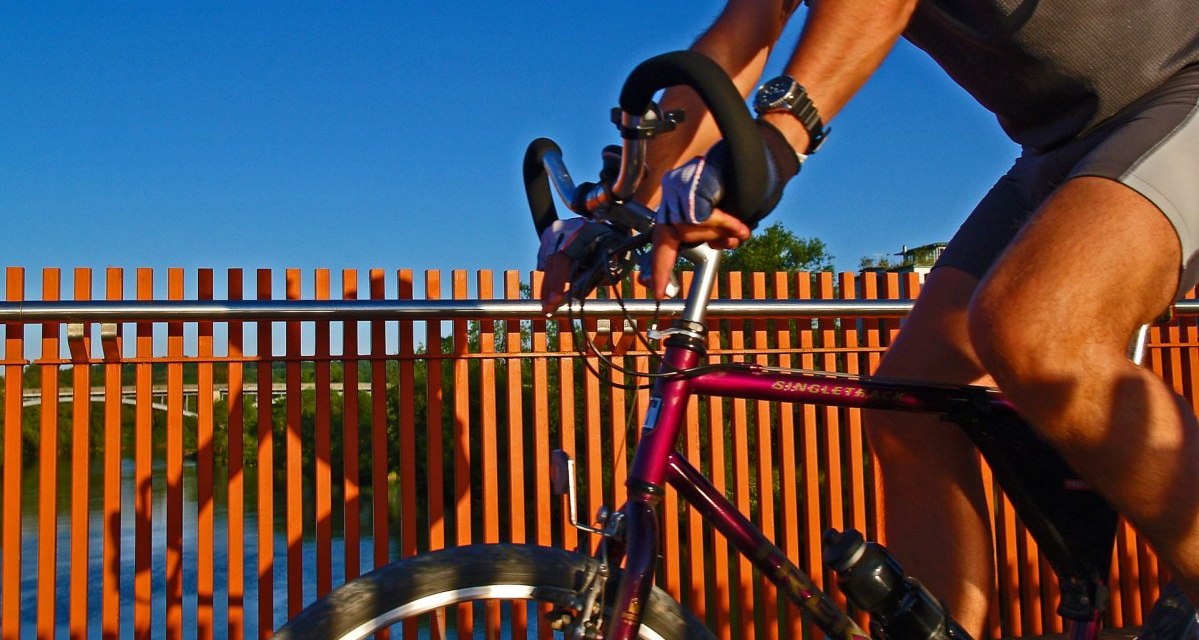 Ein Radfahrer in Sportkleidung f&auml;hrt &uuml;ber eine Br&uuml;cke mit orangefarbenem Gel&auml;nder, blauer Himmel im Hintergrund., &copy; Thomas Krebs