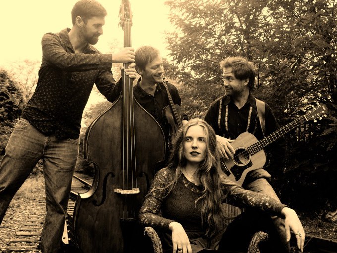 Ein Jazz-Quartett posiert im Freien. Eine Frau sitzt, während drei Männer mit Kontrabass und Gitarre um sie herumstehen. Sepia-Ton., © Stadt Murrhardt Ein Jazz-Quartett posiert im Freien. Eine Frau sitzt, während drei Männer mit Kontrabass und Gitarre um sie herumstehen. Sepia-Ton., © Stadt Murrhardt