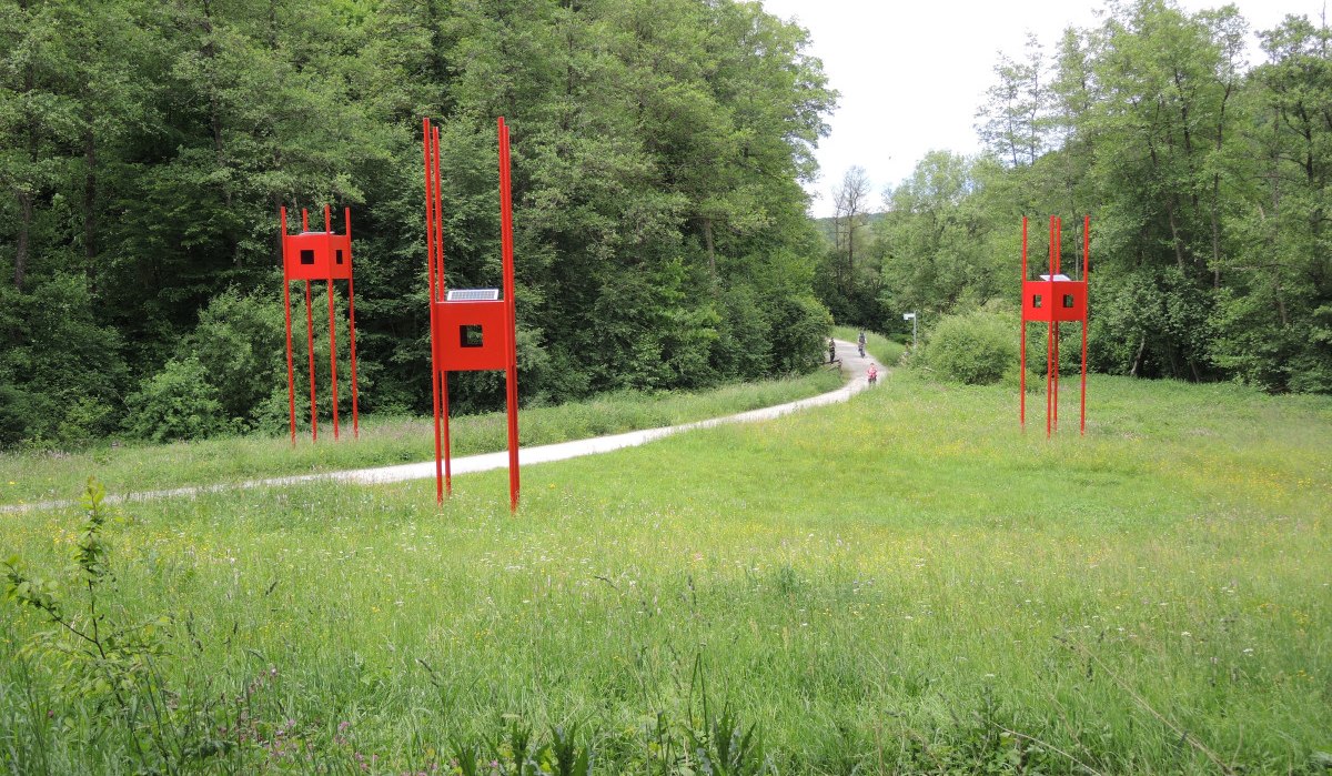 Rote, turmartige Installationen stehen auf einer grünen Wiese, umgeben von Wald. Ein Weg führt durch die Landschaft., © Natur.Nah. Schönbuch & Heckengäu Rote, turmartige Installationen stehen auf einer grünen Wiese, umgeben von Wald. Ein Weg führt durch die Landschaft., © Natur.Nah. Schönbuch & Heckengäu
