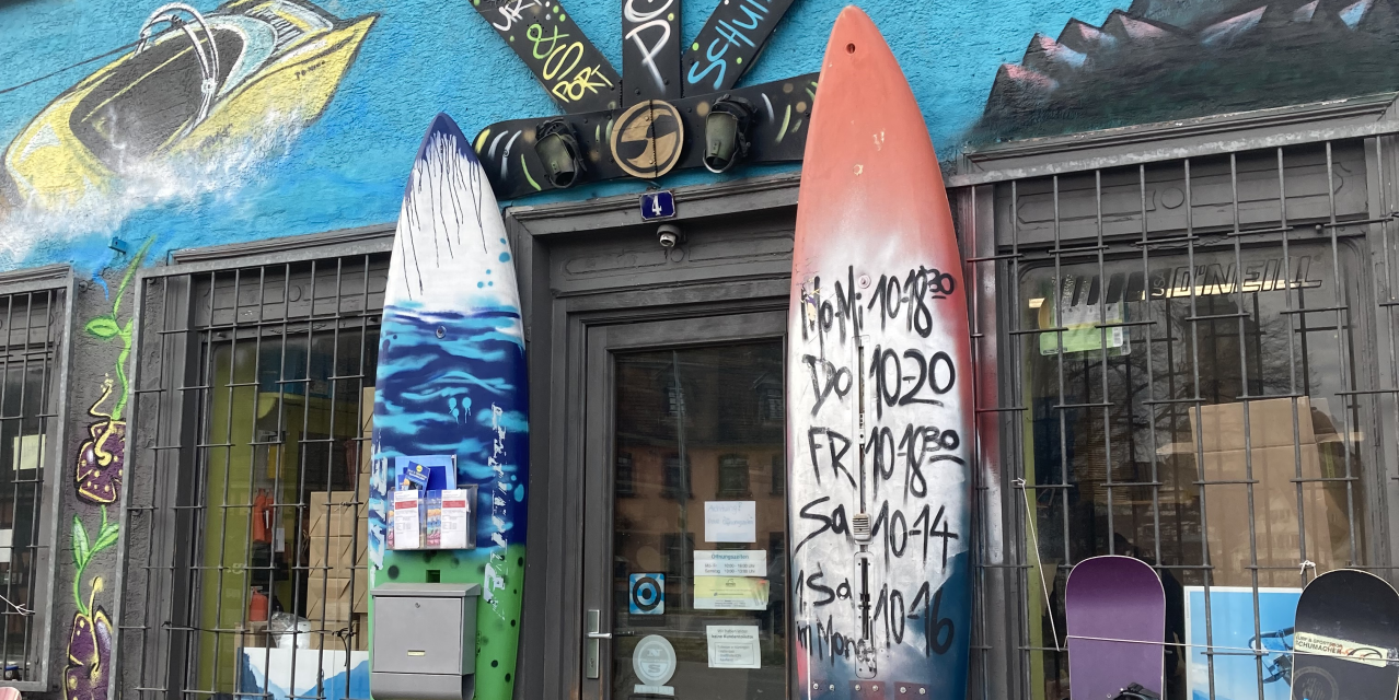 Surf- und Sportshop mit bunter Fassade, Surfbrettern und Snowboards vor dem Eingang. Graffiti und Wandmalereien schmücken das Gebäude., © L. Besmer Surf- und Sportshop mit bunter Fassade, Surfbrettern und Snowboards vor dem Eingang. Graffiti und Wandmalereien schmücken das Gebäude., © L. Besmer
