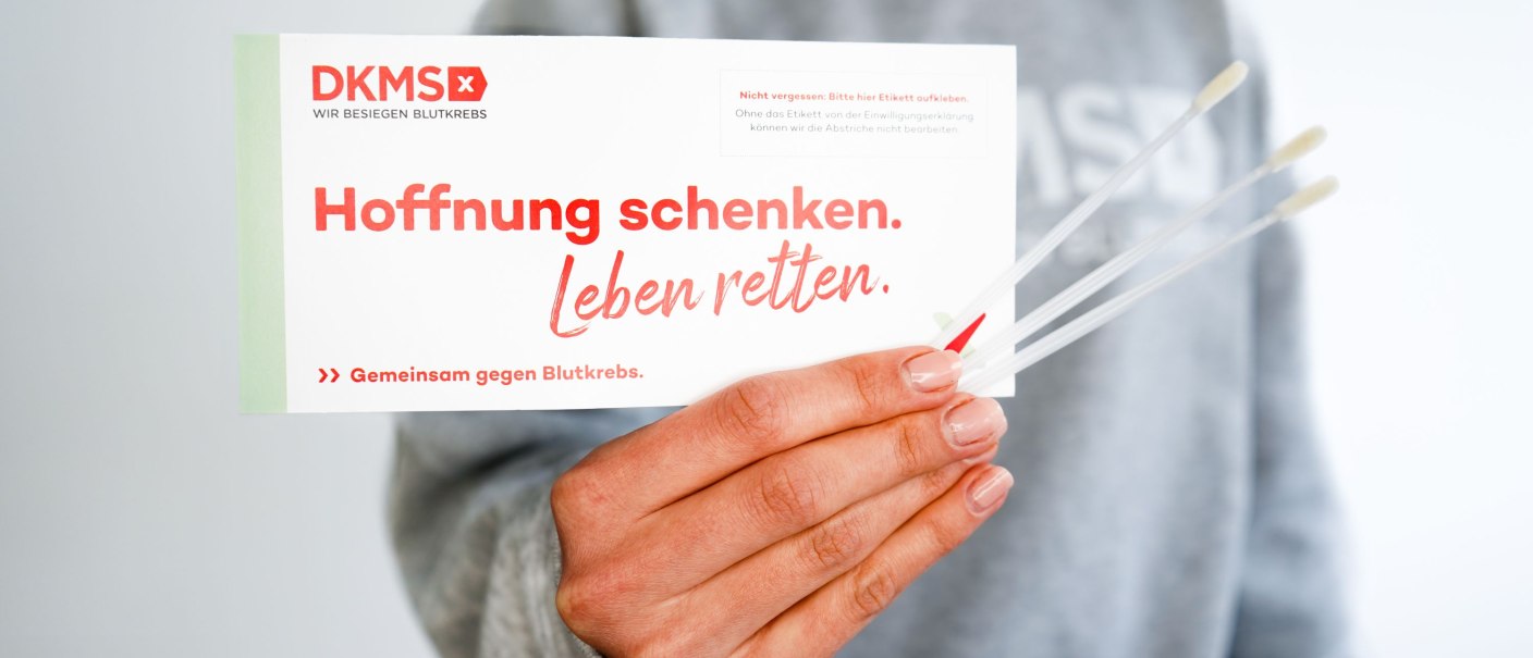 Hand, die ein DKMS-Registrierungsset hält - drei Wattestäbchen und einen Umschlag mit der Aufschrift "Hoffnung schenken. Leben retten.", © DKMS