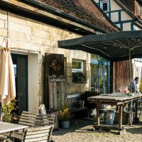 Gemütlicher Café-Außenbereich mit Holzmöbeln und Sonnenschirm, umgeben von Fachwerkhäusern und herbstlicher Landschaft., © Stuttgart-Marketing GmbH, Sarah Schmid Gemütlicher Café-Außenbereich mit Holzmöbeln und Sonnenschirm, umgeben von Fachwerkhäusern und herbstlicher Landschaft., © Stuttgart-Marketing GmbH, Sarah Schmid