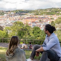 Zwei Personen sitzen auf einer Wiese und schauen auf die Stadt Stuttgart. Im Hintergrund sind H&uuml;gel und Geb&auml;ude zu sehen, darunter der Fernsehturm., &copy; SMG, Martina Denker