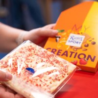 Person hält eine Tafel weiße Schokolade mit roten Streuseln und eine Verpackung mit 'My Creation' von Ritter Sport., © Alfred Ritter GmbH &amp; Co. KG | Waldenbuch