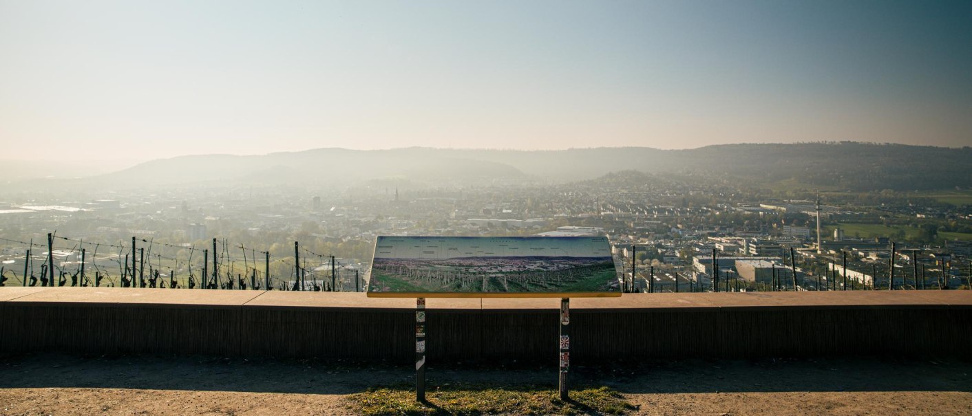 Blick vom Grafenberg auf Schorndorf mit einer Infotafel im Vordergrund. Die Stadt liegt unter einem leicht bewölkten Himmel., © Stuttgart-Marketing GmbH, Sarah Schmid