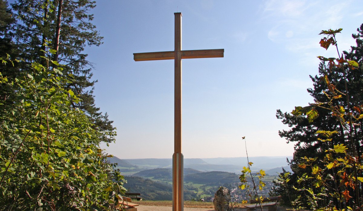 Ein großes Holzkreuz auf einem Hügel mit Blick auf eine weite Landschaft, umgeben von Bäumen und Bänken., © Foto: Frieder Kopper