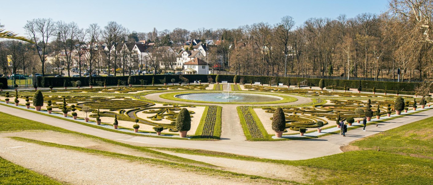 Der Barockgarten in Ludwigsburg zeigt kunstvoll geschnittene Hecken und einen zentralen Brunnen, umgeben von Bäumen und Gebäuden im Hintergrund., © Stuttgart-Marketing GmbH, Sarah Schmid