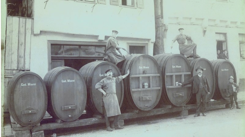 Männer posieren vor großen Holzfässern mit der Aufschrift 'Gust. Maurer'. Personen schauen aus den Fenstern eines Gebäudes., © Stadt Leonberg Männer posieren vor großen Holzfässern mit der Aufschrift 'Gust. Maurer'. Personen schauen aus den Fenstern eines Gebäudes., © Stadt Leonberg