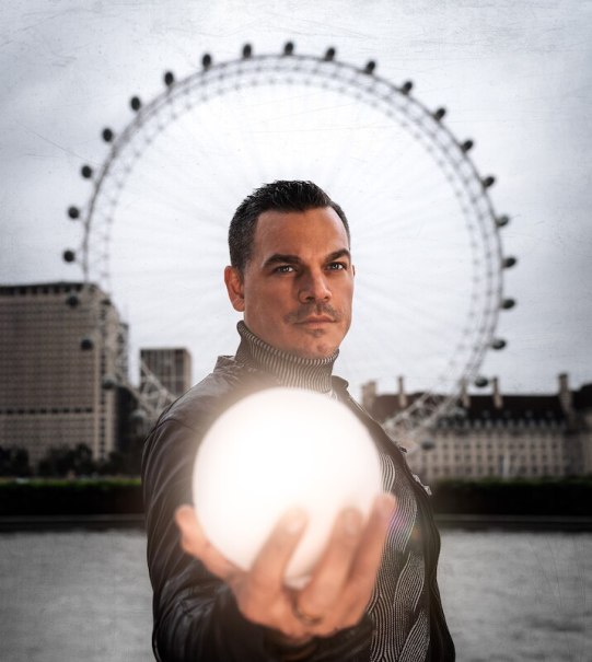 Ein Mann in Lederjacke hält eine leuchtende Kugel vor dem London Eye. Der Himmel ist bewölkt, und die Szene wirkt mystisch., © Mercedes-Benz AG
