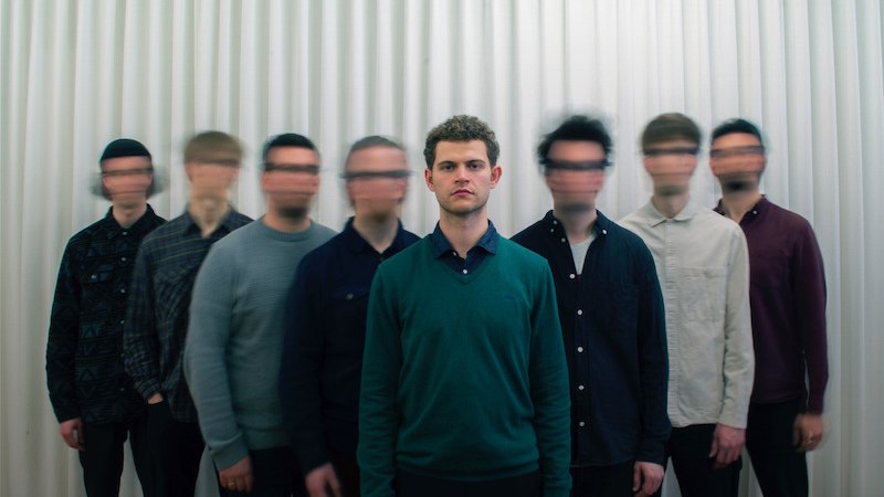 Ein Mann steht klar im Vordergrund, w&auml;hrend sieben weitere M&auml;nner unscharf im Hintergrund vor einem wei&szlig;en Vorhang stehen., &copy; Interessengemeinschaft Kultur Sindelfingen / B&ouml;blingen e.V.