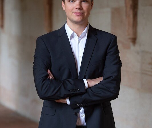 Ein Mann in einem schwarzen Anzug steht mit verschr&auml;nkten Armen in einem &uuml;berdachten Gang mit Steinw&auml;nden., &copy; Stadtverwaltung Vaihingen an der Enz