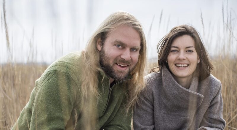 Ein Mann mit langen Haaren und eine Frau mit dunklem Haar l&auml;cheln in die Kamera. Sie befinden sich in einer nat&uuml;rlichen Umgebung mit hohen Gr&auml;sern., &copy; Kulturstiftung Hohenlohe