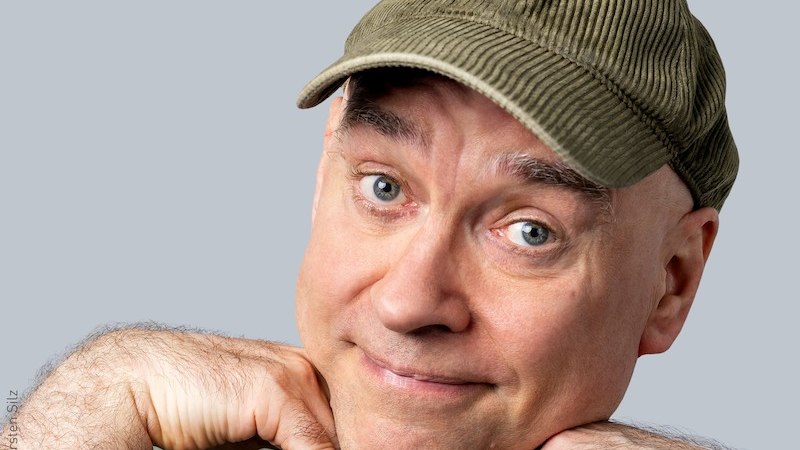 Ein Mann mit grüner Mütze stützt sein Kinn auf die Hände und lächelt in die Kamera. Hintergrund ist einfarbig hellgrau., © Stadt Kornwestheim Kulturmanagement Ein Mann mit grüner Mütze stützt sein Kinn auf die Hände und lächelt in die Kamera. Hintergrund ist einfarbig hellgrau., © Stadt Kornwestheim Kulturmanagement