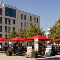 Moderne Wohngebäude in Stuttgart Killesberghöhe, mit roten Sonnenschirmen und Menschen auf einem Platz bei sonnigem Wetter., © Stuttgart-Marketing GmbH, Sarah Schmid