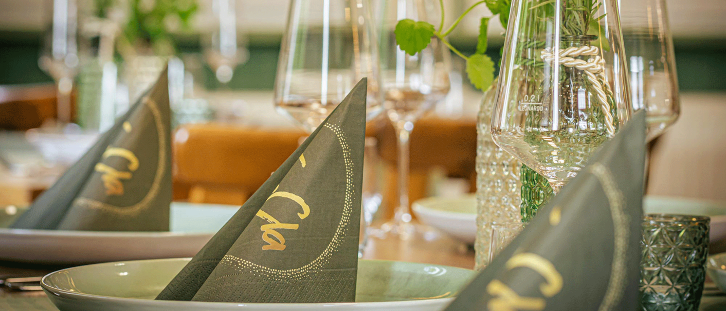 Ein elegant gedeckter Tisch mit gefalteten Servietten, Gl&auml;sern und dekorativen Elementen. Die Servietten tragen den Schriftzug 'Cla'., &copy; FreCla Gastronomiebetriebe GmbH