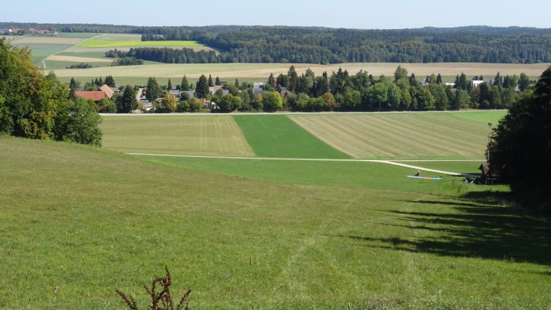 Gr&uuml;ne Wiesen und Felder erstrecken sich bis zu einem Dorf am Waldrand unter blauem Himmel., &copy; Foto: Cornelia Steinbach