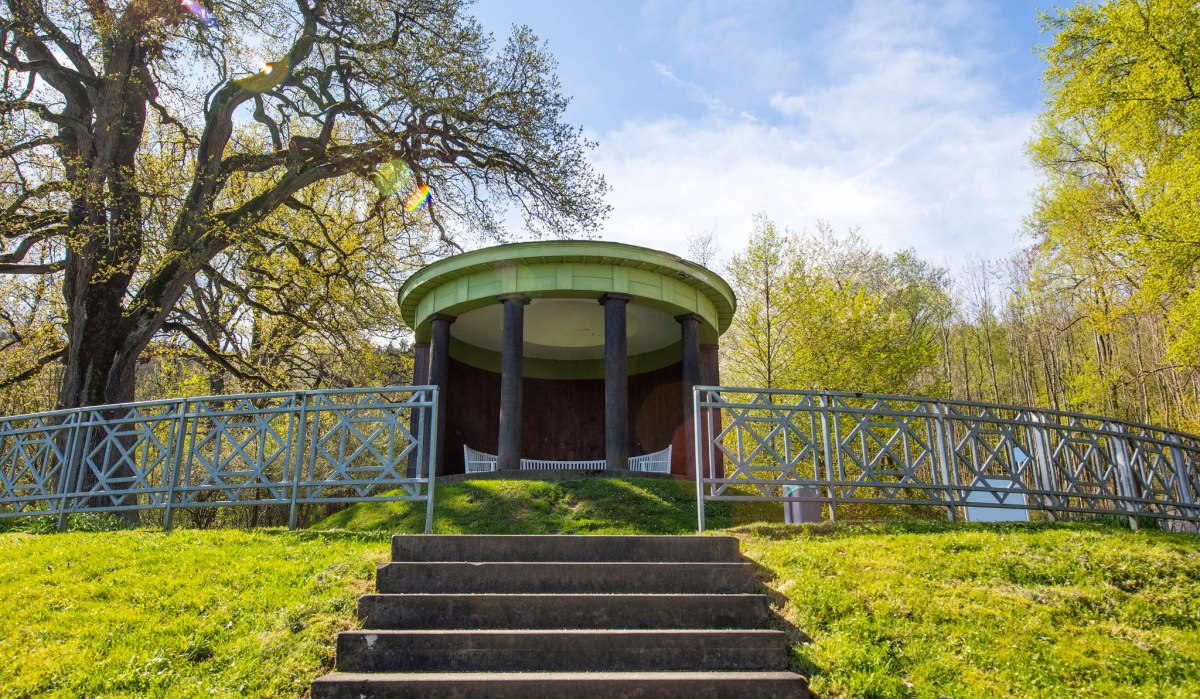 Ein runder Pavillon mit Säulen steht auf einem Hügel, umgeben von Bäumen und einem Geländer. Eine Treppe führt hinauf., © Landkreis Göppingen Ein runder Pavillon mit Säulen steht auf einem Hügel, umgeben von Bäumen und einem Geländer. Eine Treppe führt hinauf., © Landkreis Göppingen