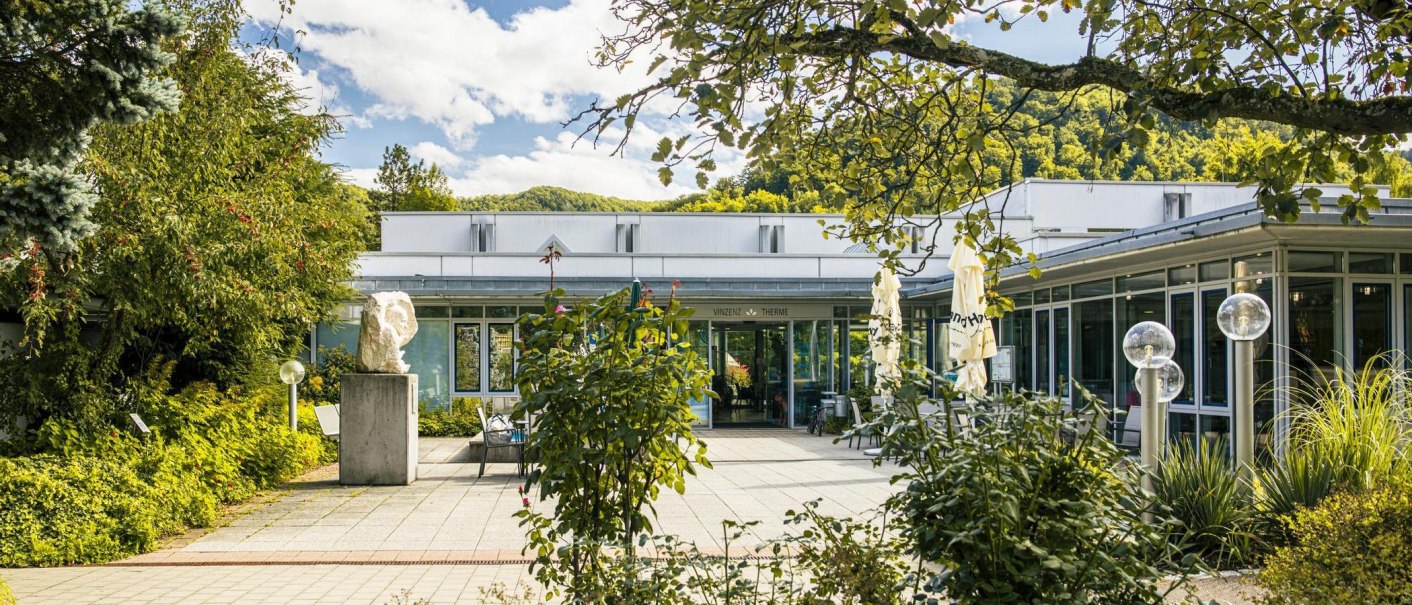 Eingang der Vinzenz Therme in Bad Ditzenbach, umgeben von &uuml;ppigem Gr&uuml;n und einem sonnigen Himmel., &copy; SMG, Sarah Schmid