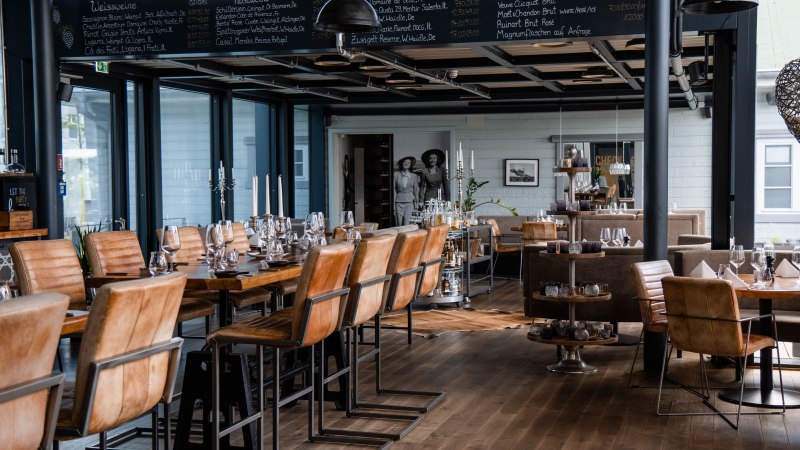Stilvolles Restaurant mit Holzb&ouml;den, Ledersesseln und gedeckten Tischen. An der Wand eine Tafel mit Weinauswahl. Elegante Atmosph&auml;re., &copy; Check Inn Restaurant