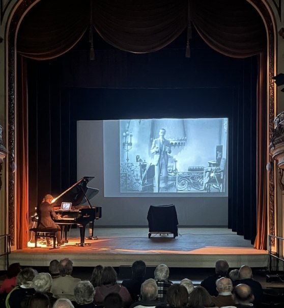 Ein Pianist begleitet live einen Stummfilm auf einer B&uuml;hne. Der Film wird auf eine Leinwand projiziert, w&auml;hrend das Publikum zuschaut., &copy; Touristik Bad Wildbad GmbH